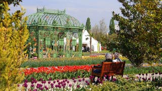 Park mit Glashaus, davor blhende Blumen